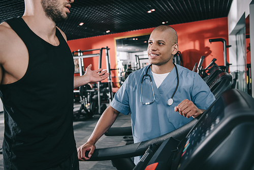 cropped view of sportsman showing shrug gesture near smiling african american doctor