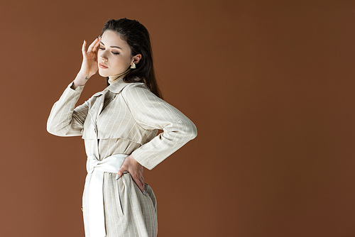 fashionable woman in trench coat isolated on brown with hand on hip