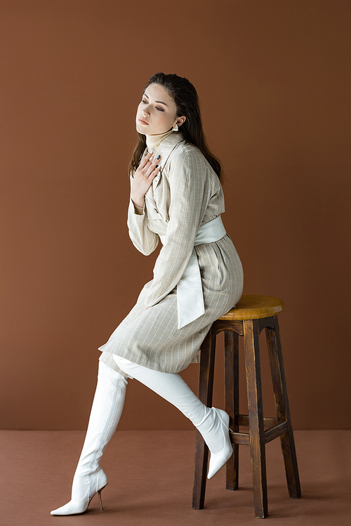 stylish woman sitting on wooden chair isolated on brown