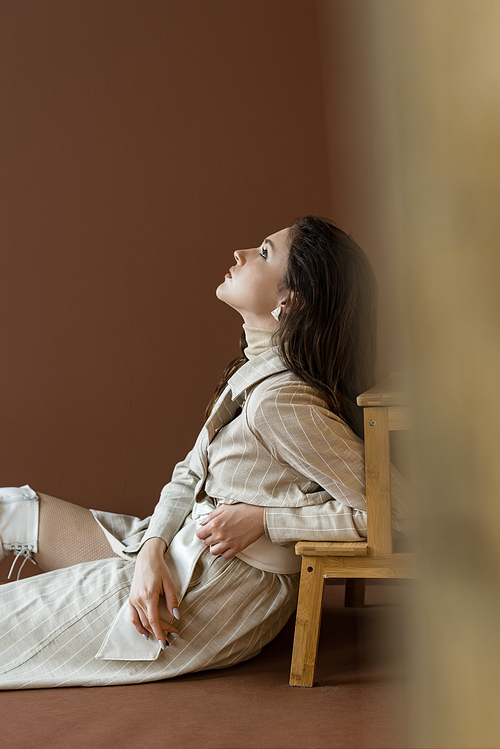 side view of beautiful and trendy woman sitting on floor, looking up