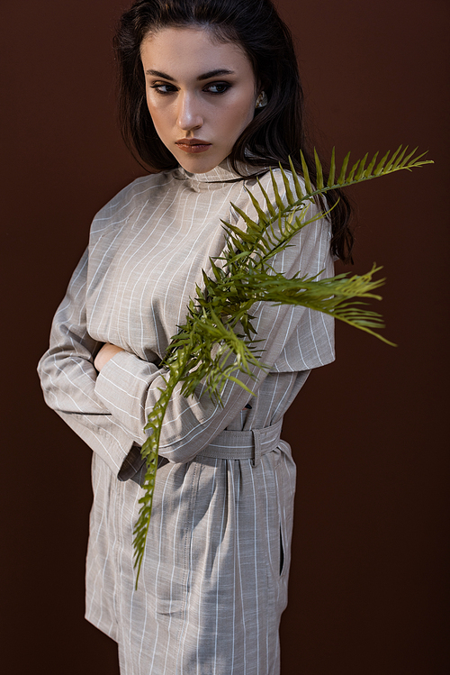 model holding fern leaves in hands, looking away, standing on brown background