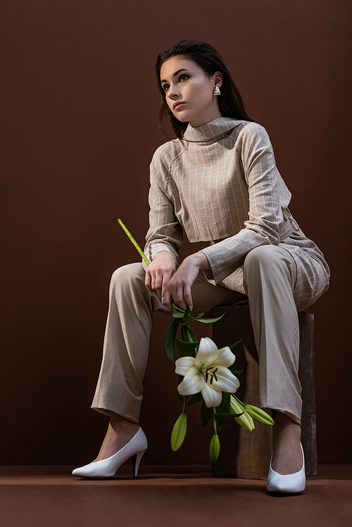 low angle view of model with flower in hands sitting on box ,looking away