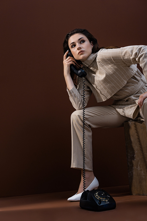 stylish woman with handset in hand looking away, sitting on box