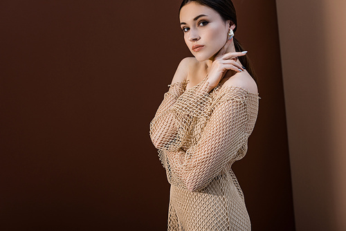 side view of attractive woman in mesh dress standing on brown background, 