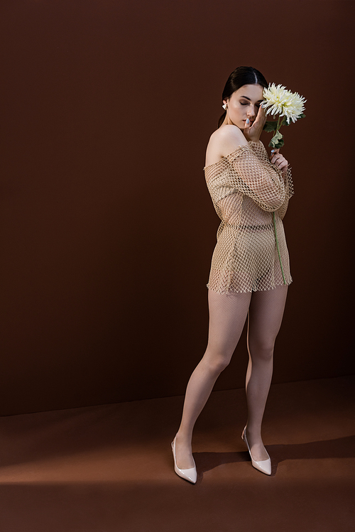 model with flower in hands closing eyes, standing on brown background