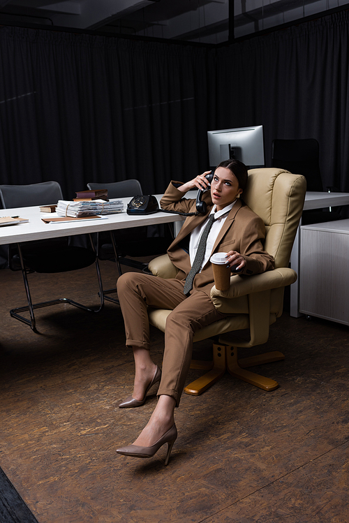 successful businesswoman talking on phone, sitting in armchair with paper cup ,looking away