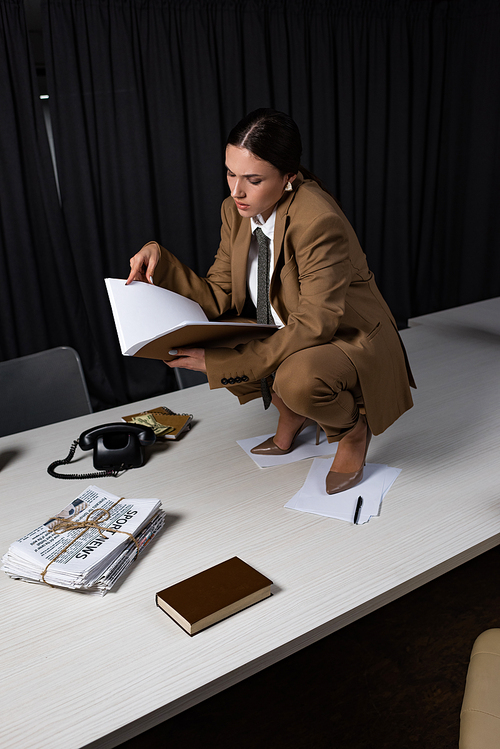 high angle view of businesswoman sitting on table, holding documents in hands