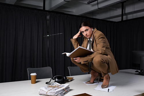 stylish businesswoman in suit sitting on table, holding documents and 