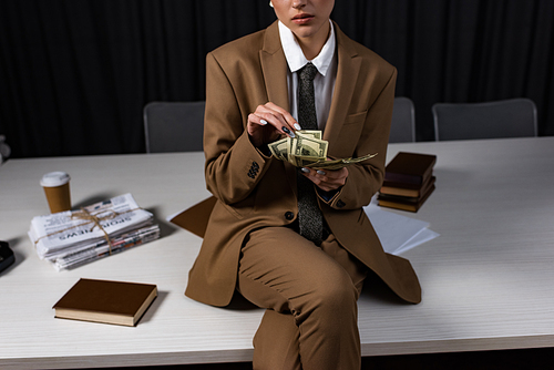cropped view of successful businesswoman sitting on table, crossing legs and counting money
