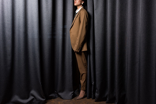 side view of fashionable model in suit standing in studio with grey curtain background