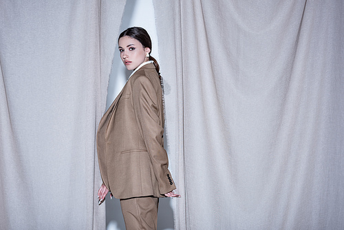 side view of successful woman in suit standing on light grey curtain background, 