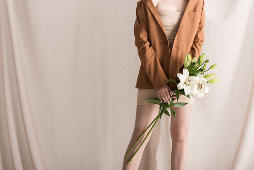 cropped view of woman holding flowers in hands, standing on curtain background