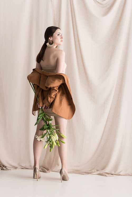 fashionable model standing on curtain background, holding flowers in hands