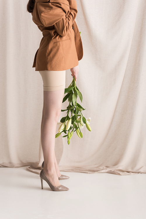 cropped view of adult woman standing on curtain background with flowers in hands