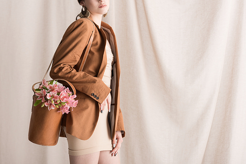cropped view of stylish woman carries flowers in bag, standing on curtain background