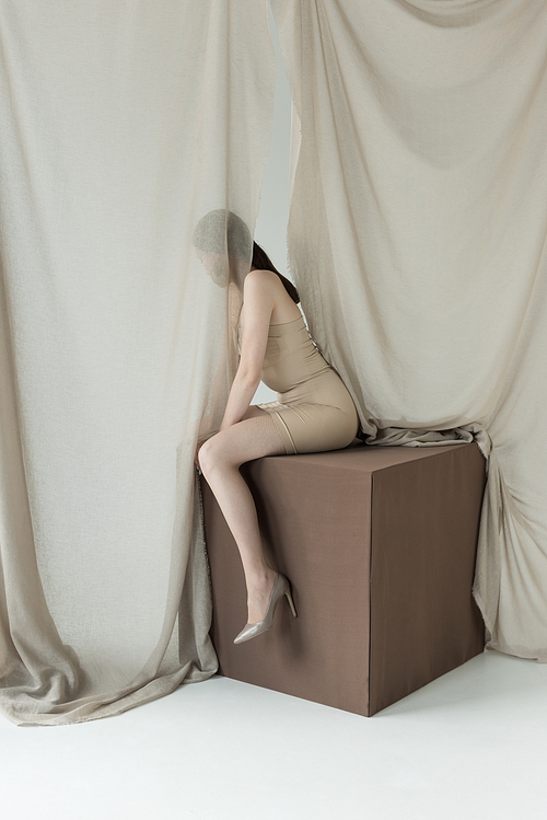 young model in dress sitting on cube behind light curtain
