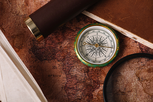 top view of compass near copy book and magnifying glass on old world map