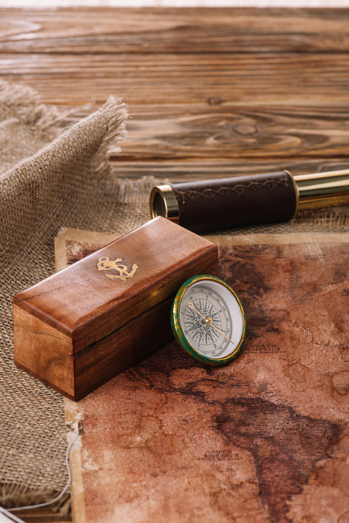 box with anchor logo near compass on wooden table with sacking and world map