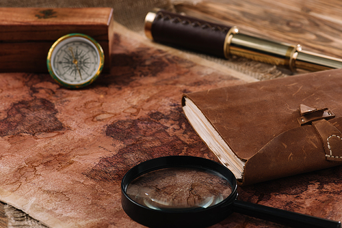 old world map with telescope, leather notebook, magnifying glass and compass on wooden surface
