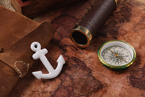 white anchor near leather copy book, compass and telescope on old world map