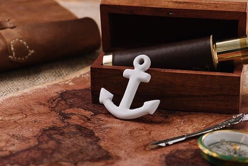 white anchor near open wooden box with telescope on world map