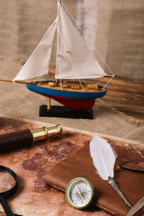 miniature ship, telescope, magnifying glass, leather copy book and nib on old world map and hessian