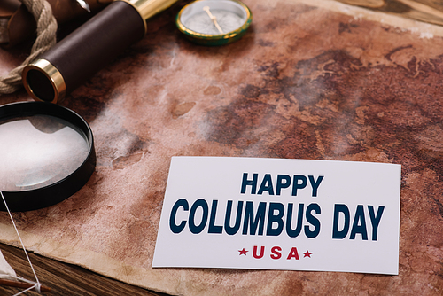 card with happy Columbus Day inscription near compass and magnifying glass on old world map