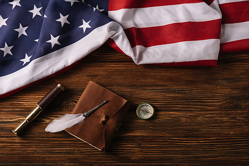 top view of leather notebook, telescope, nib and compass on wooden surface with American national flag