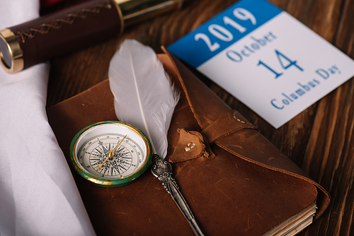 calendar with October 14 date near leather notebook with nib and compass on wooden surface