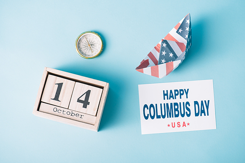 top view of calendar with October 14 date near paper boat with American flag pattern, compass and card with happy Columbus Day inscription on blue background