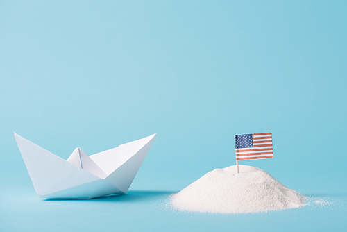 paper boat near American national flag in white sand on blue background