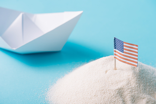 white paper boat near sand with American national flag on blue background