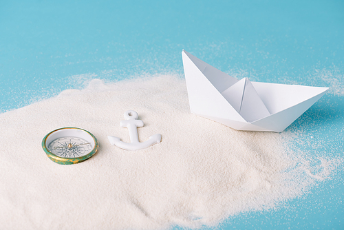 sand with paper boat, compass and anchor on blue background