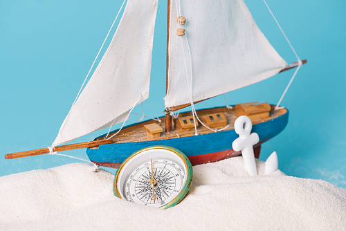 close up view of decorative ship near anchor and compass in white sand isolated on blue