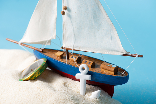 miniature ship near compass and anchor in white sand isolated on blue