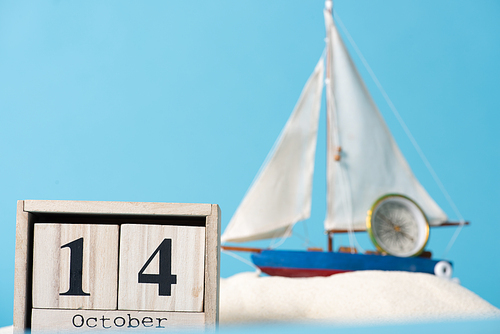 wooden calendar with 14 October date near decorative ship and compass  in white sand isolated on blue
