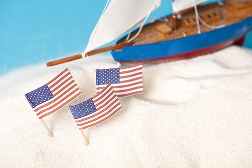 American national flags in white sand near miniature ship isolated on blue