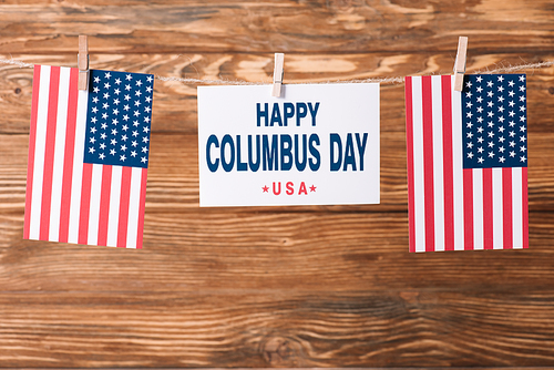card with happy Columbus day inscription between American national flags on wooden surface