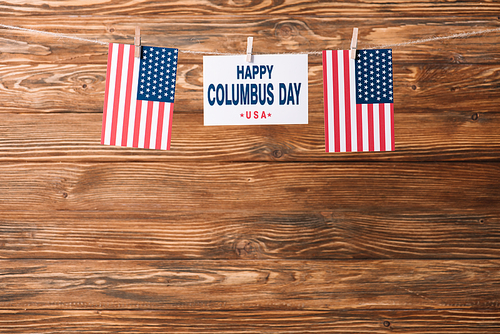 card with happy Columbus day inscription between national flags of America on wooden surface