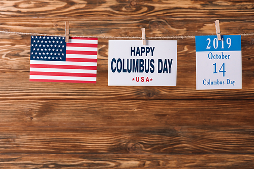 card with happy Columbus day inscription near American national flag and calendar paper sheet with 14 October date on wooden surface
