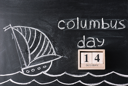 wooden calendar with October 14 date on chalkboard with ship drawing and Columbus Day inscription