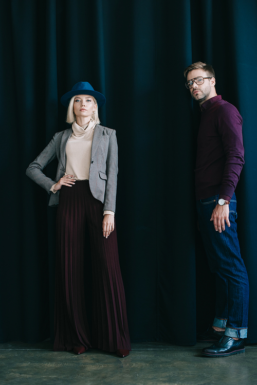 full length view of stylish young man in glasses and blonde woman in hat near curtain