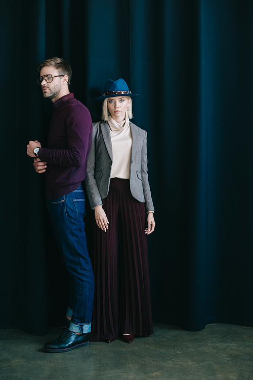 full length view of stylish young man in glasses and blonde woman in hat near curtain