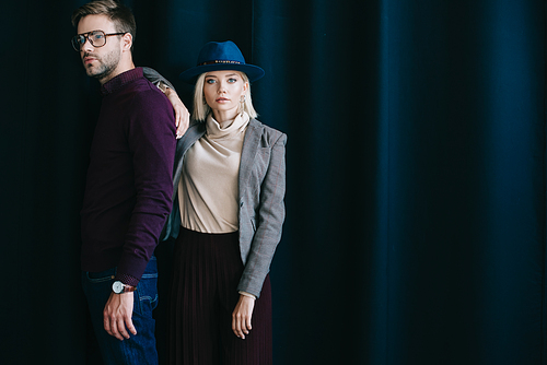 stylish young man in glasses and blonde woman in hat near curtain