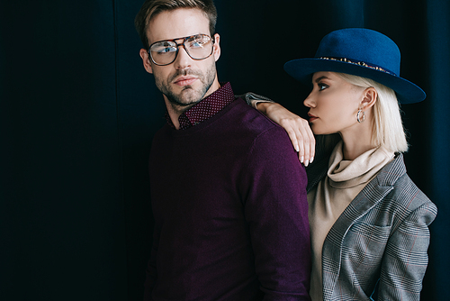 stylish young man in glasses and blonde woman in hat near curtain