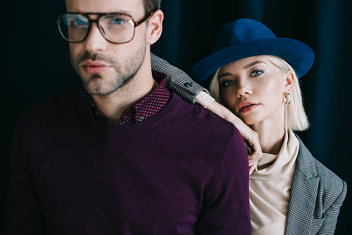 stylish young man in glasses and blonde woman in hat  near curtain