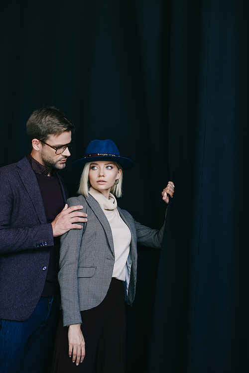 elegant young woman in hat and man in glasses near curtain