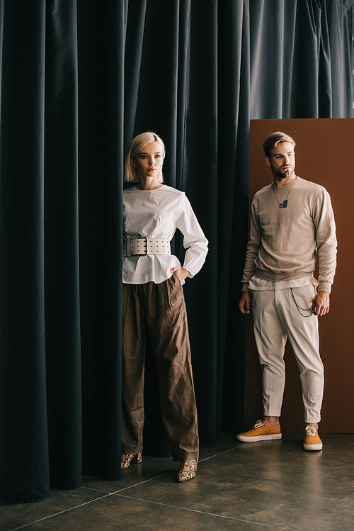 full length view of elegant blonde woman and bearded man standing near curtain