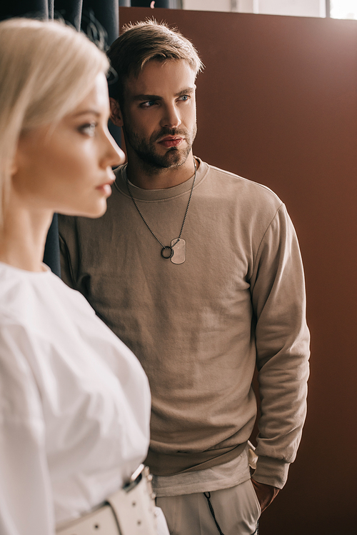 selective focus of attractive blonde girl and bearded young man with hand in pocket on brown