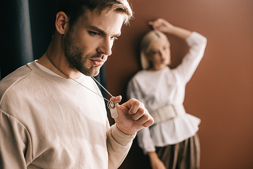 pensive young man touching pendants and blonde girl on brown